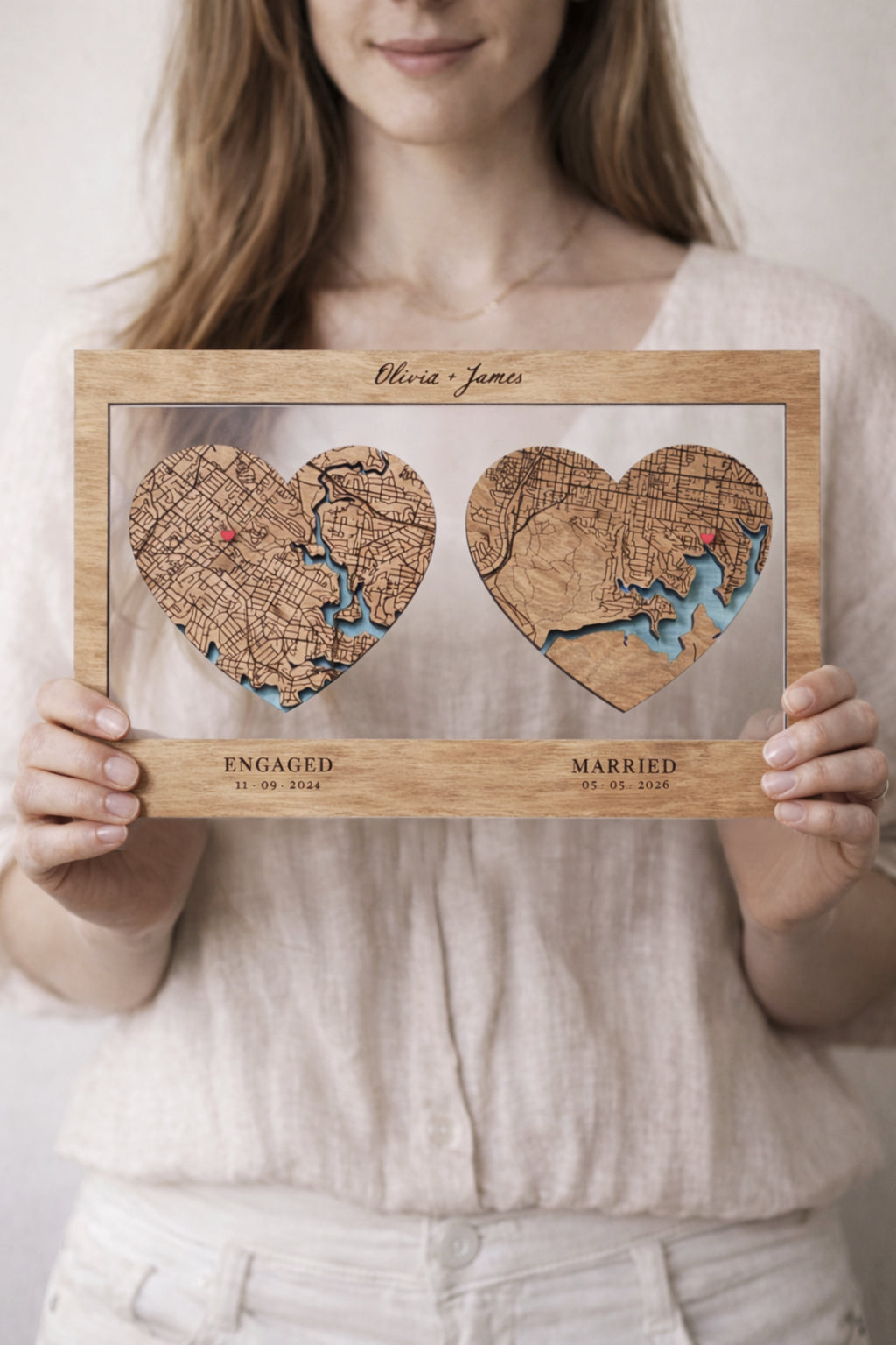 Woman holding personalised wooden engagement and wedding map gift with two heart shaped locations and engraved names Olivia and James